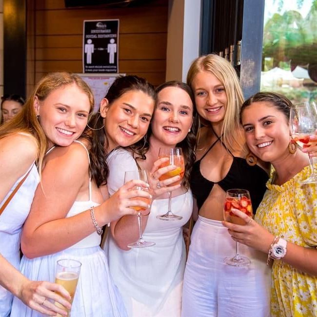A group of women are posing for a picture while holding wine glasses.