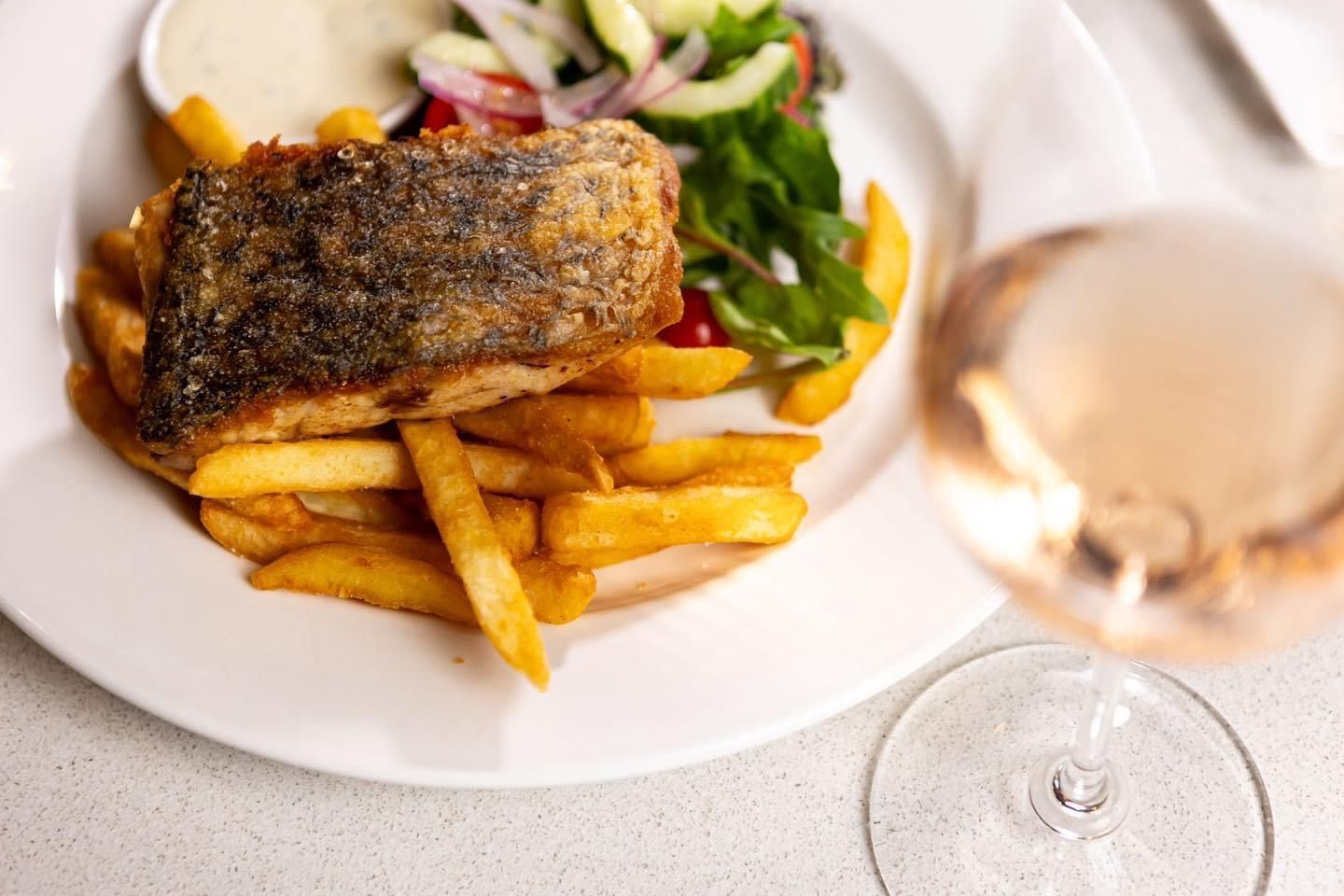 Fried fish with fries, salad, and rose wine on a white plate.
