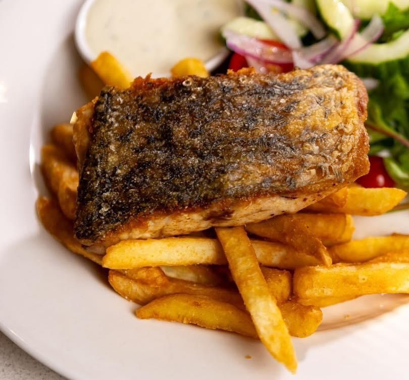 Pan-seared fish fillet on fries with a side salad and lemon wedge on a white plate