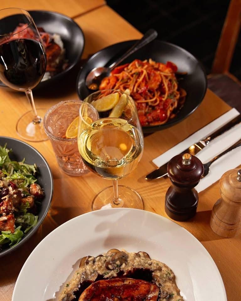 Dining table with pasta, salad, wine glasses, and condiments in a warm restaurant setting