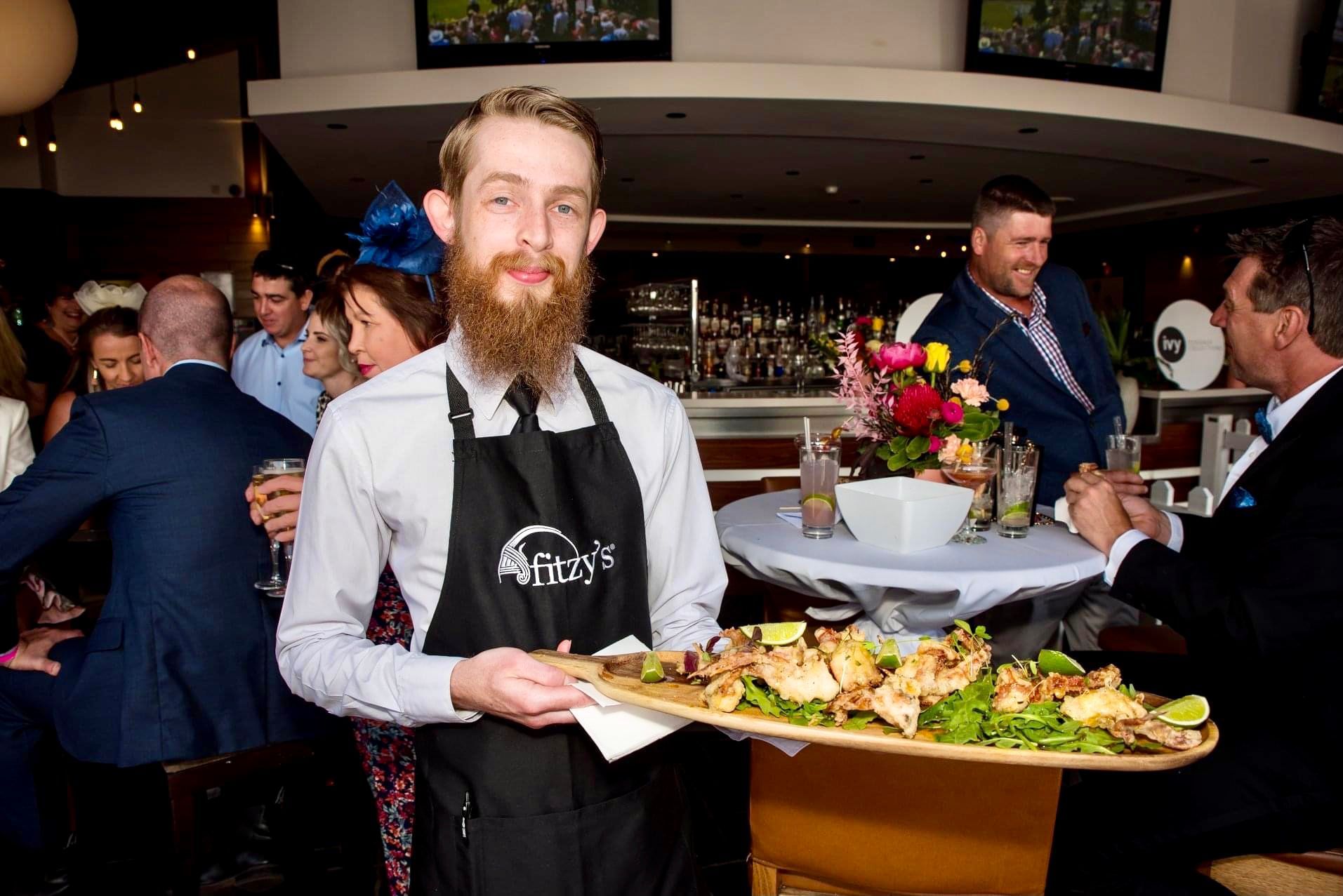 A man with a beard is holding a tray of food in a restaurant.