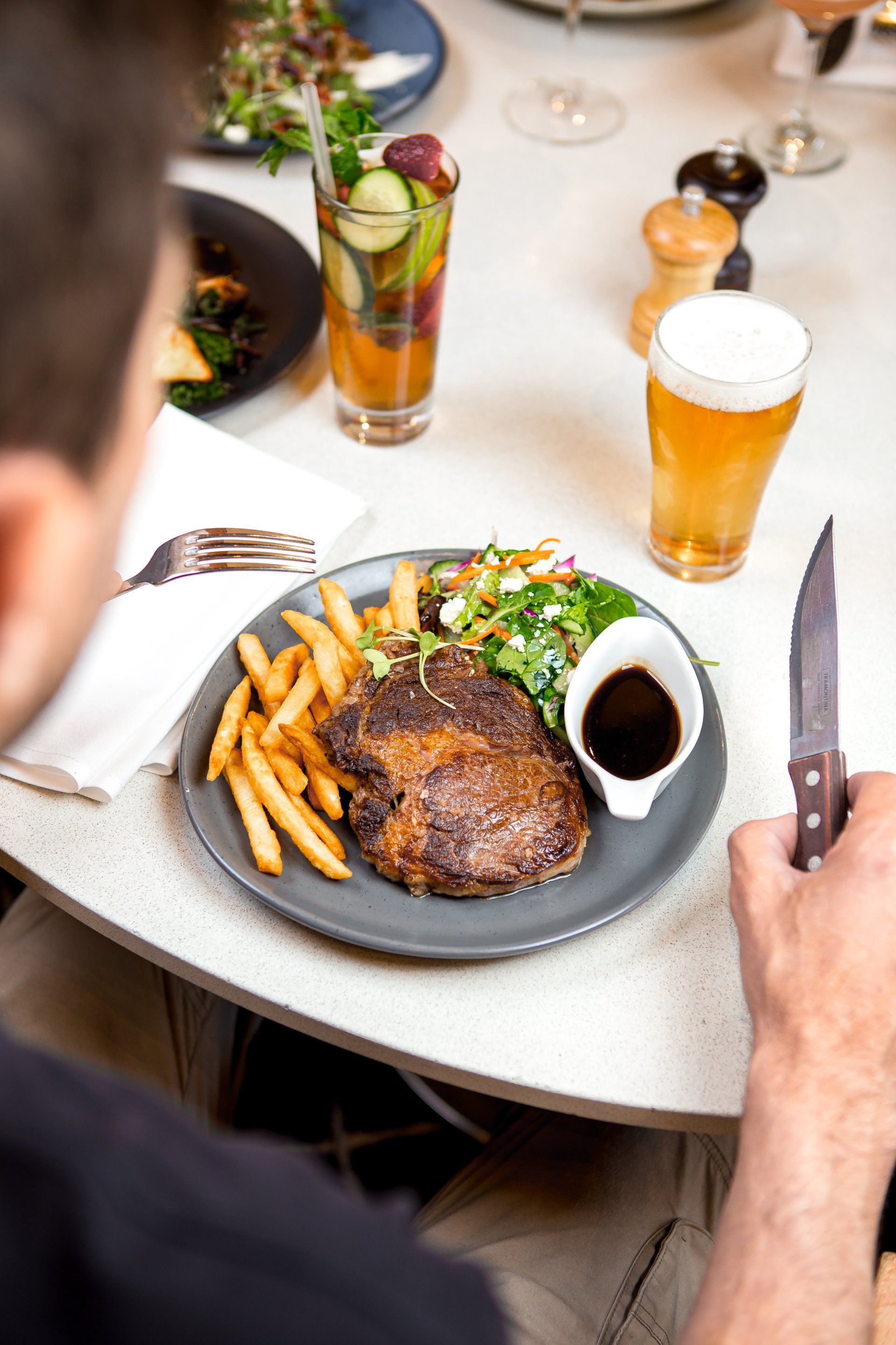 A man is sitting at a table with a plate of food and a glass of beer.