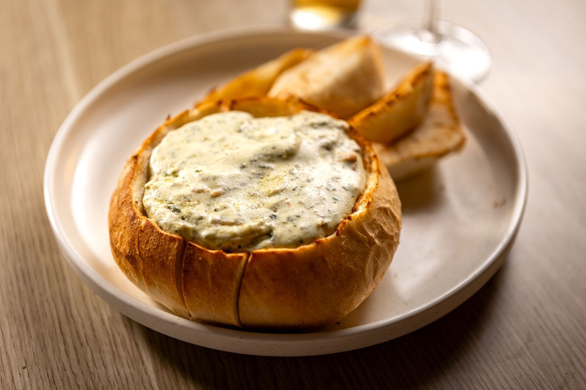 Spinach and artichoke dip served in a bread bowl with bread wedges on a white plate.
