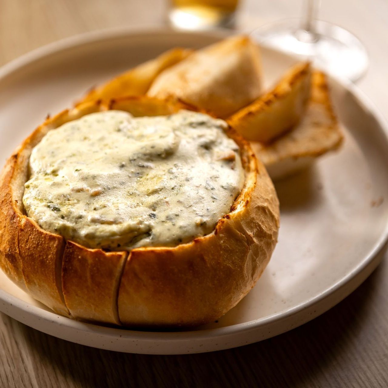 Spinach, bacon and cream cheese dip served in a cob loaf bread bowl with toasted bread wedges on a white plate.