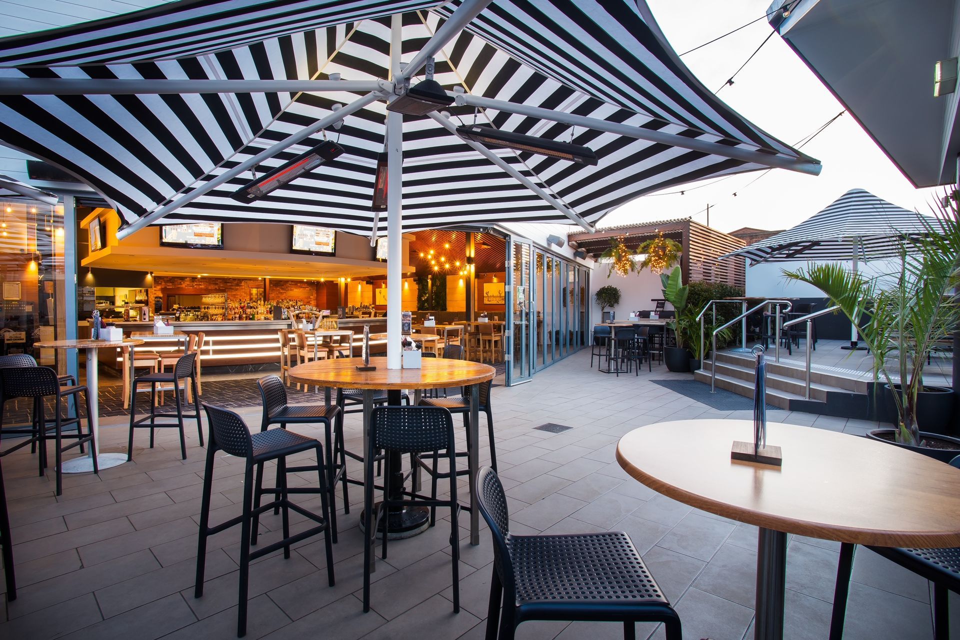 A restaurant with tables and chairs under striped umbrellas.