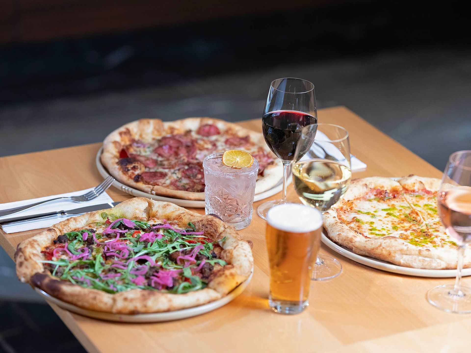 Assorted pizzas and drinks on a wooden table in a restaurant setting