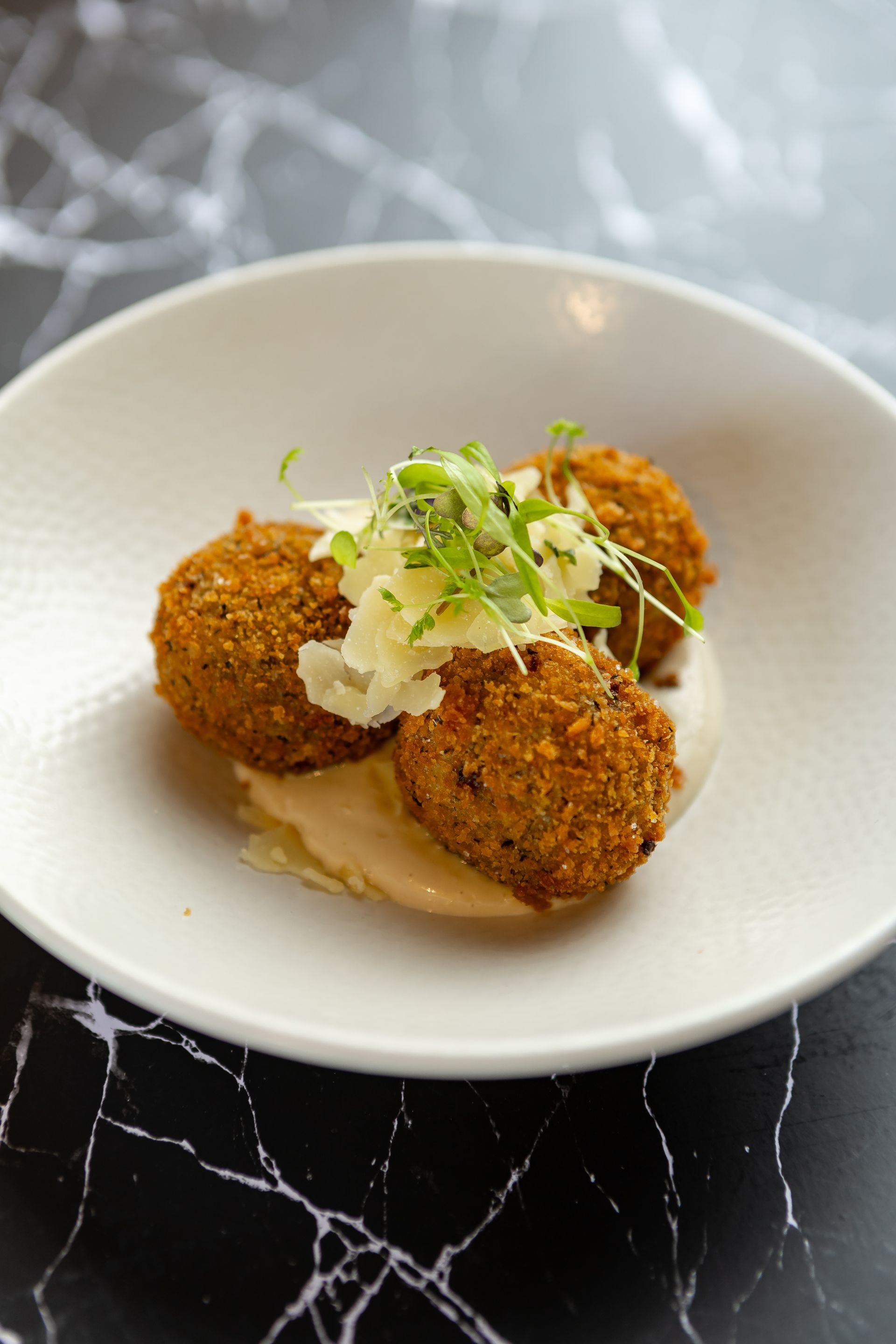 Three crispy croquettes garnished with microgreens on a white bowl, on a black marble table