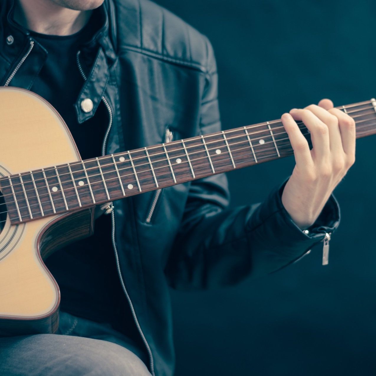 A man in a leather jacket is playing an acoustic guitar