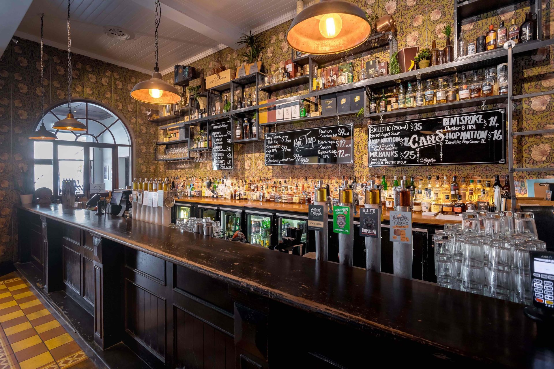 A long bar in a restaurant filled with lots of bottles and glasses.