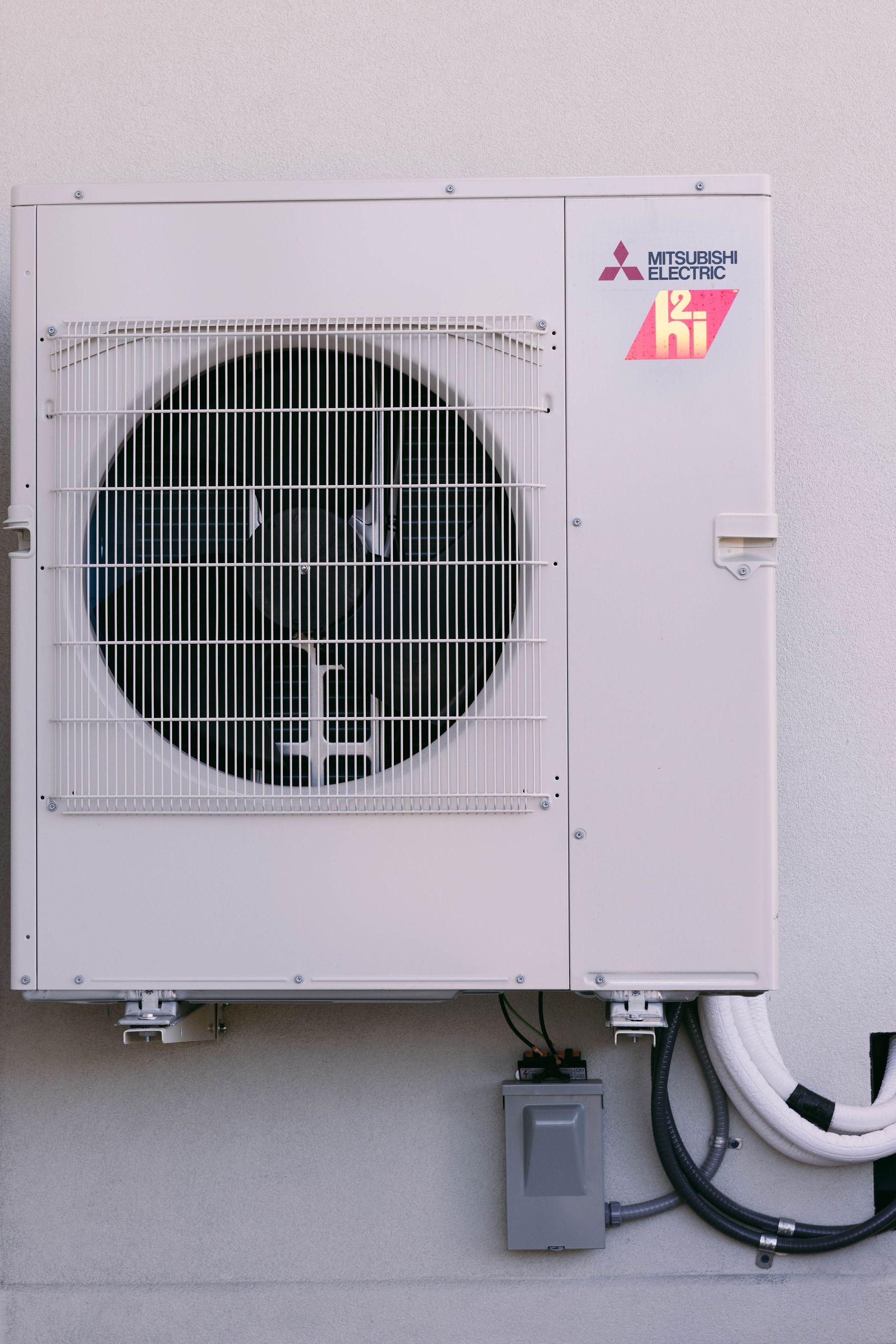 Wall-mounted outdoor air conditioner unit with a large fan and attached pipes on a building exterior