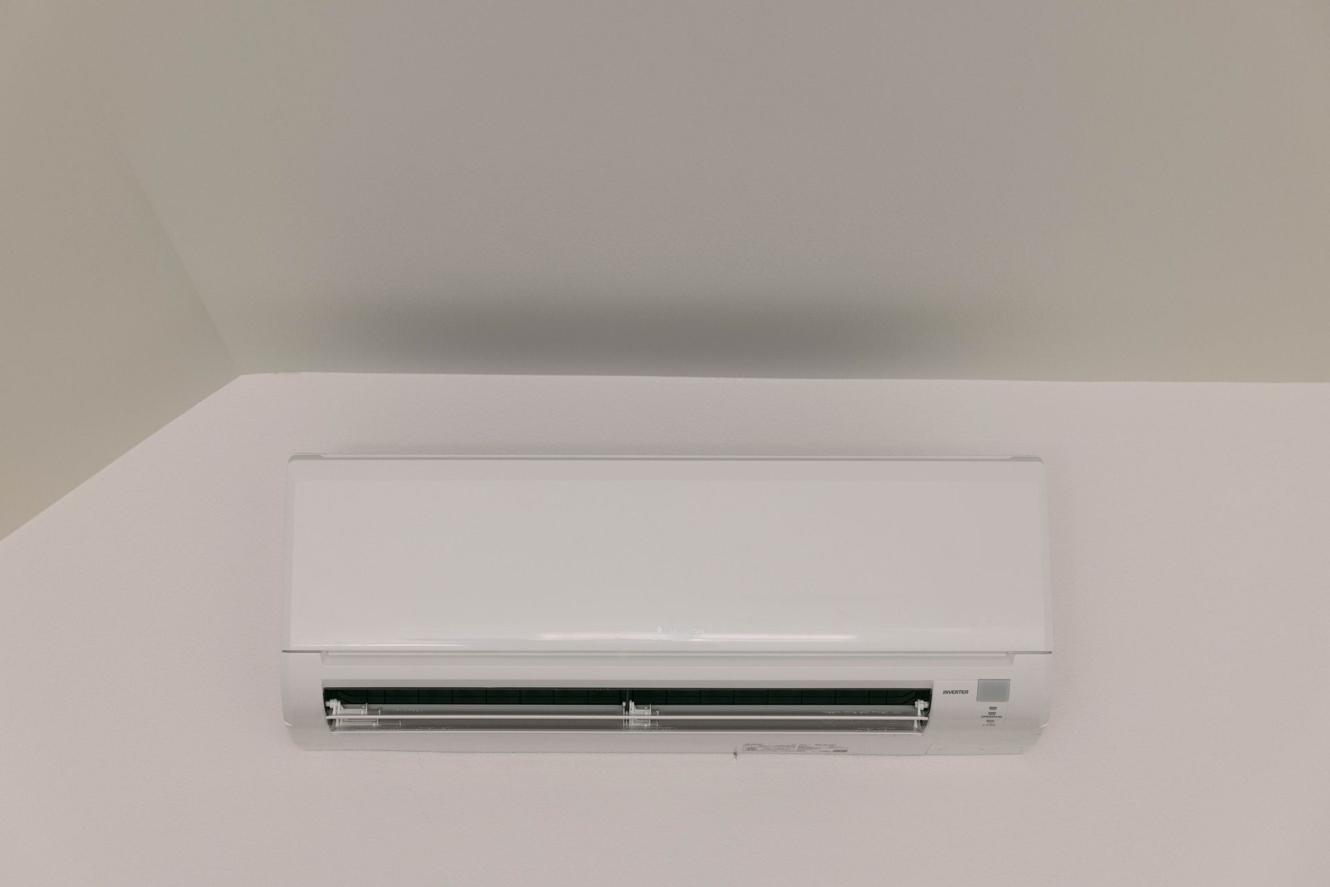 White wall-mounted air conditioner on a pale gray wall and ceiling corner
