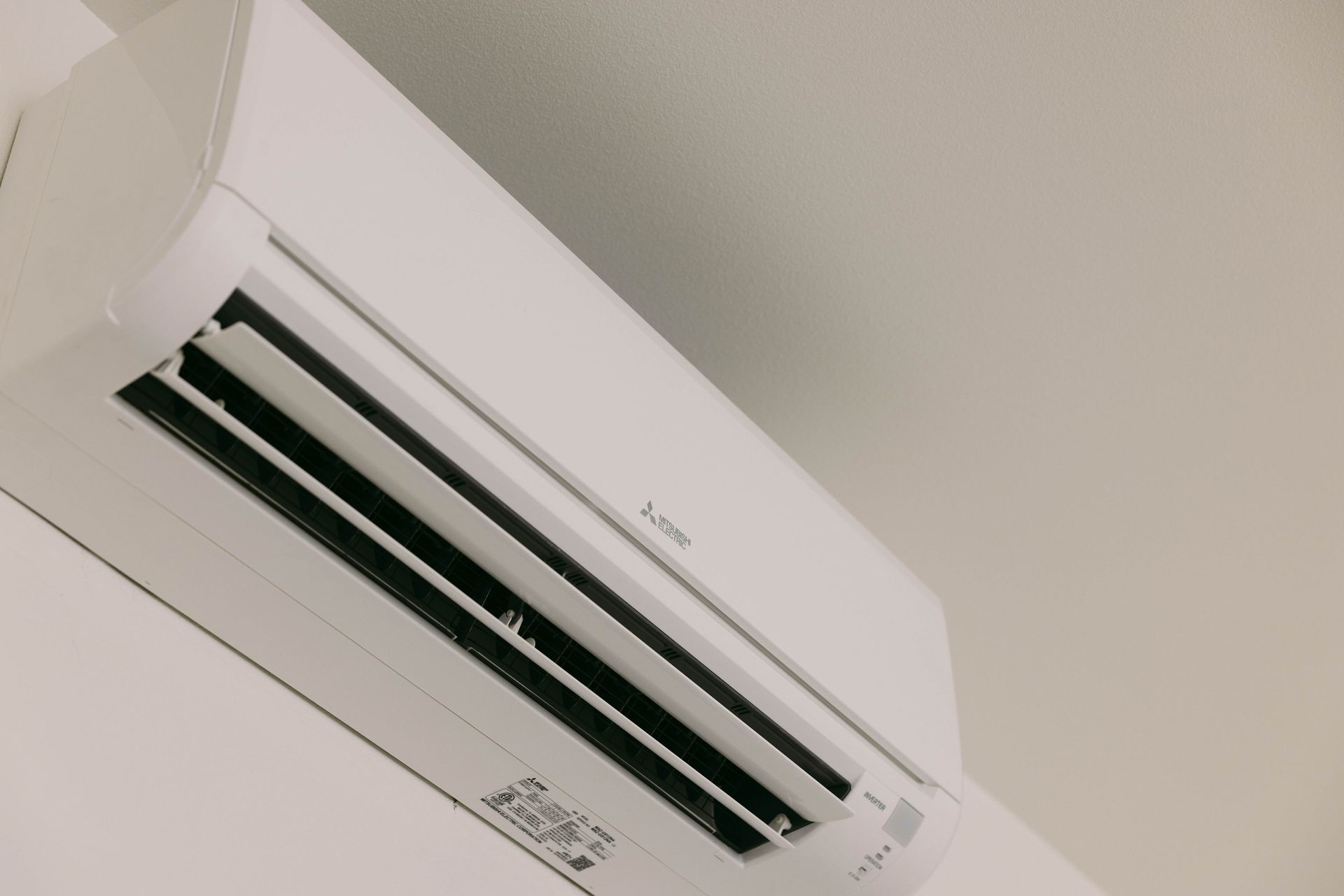 White wall-mounted air conditioner on a ceiling, angled view against a light-colored room.