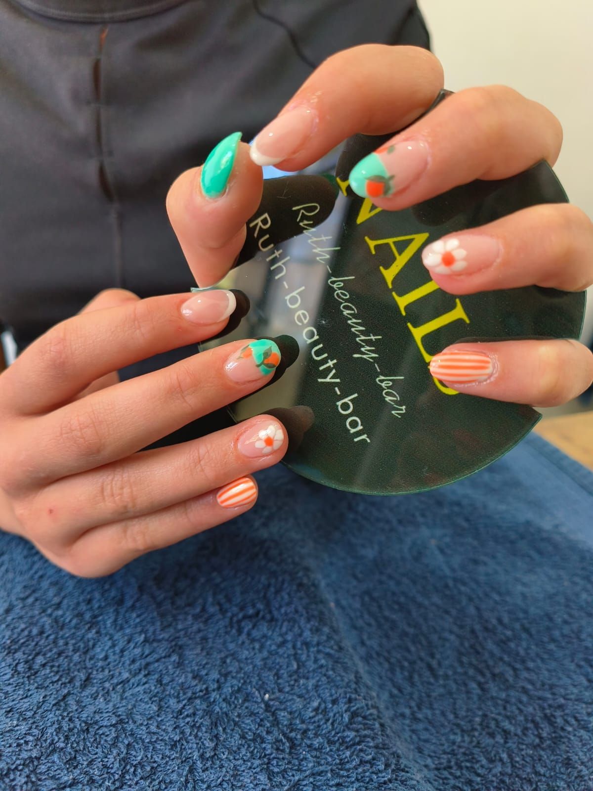Hands hold a beauty salon card displaying multi-colored French tip nails with floral, striped, and solid patterns.