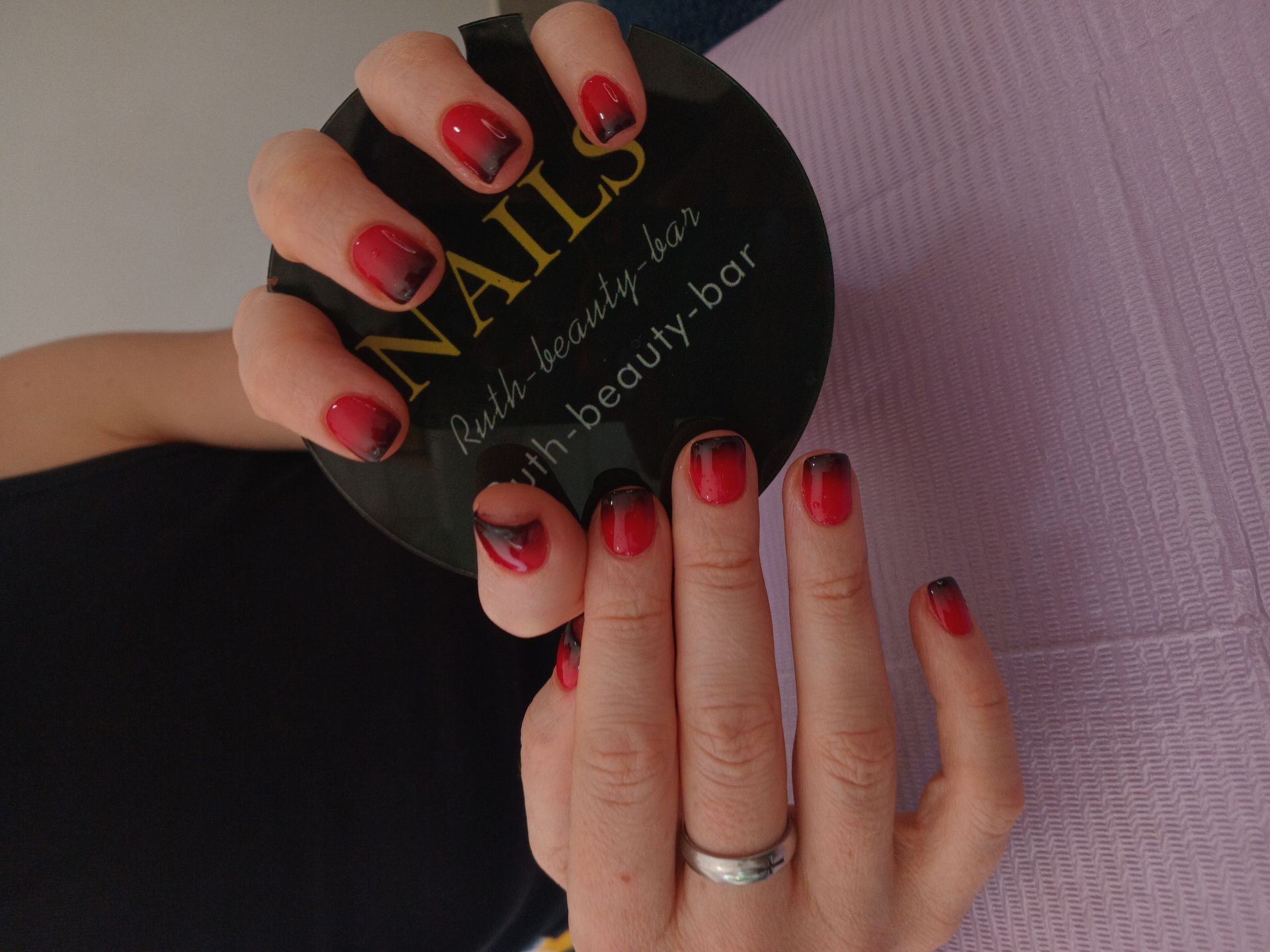 A person’s hands showcasing a red and black ombre manicure while holding a circular 