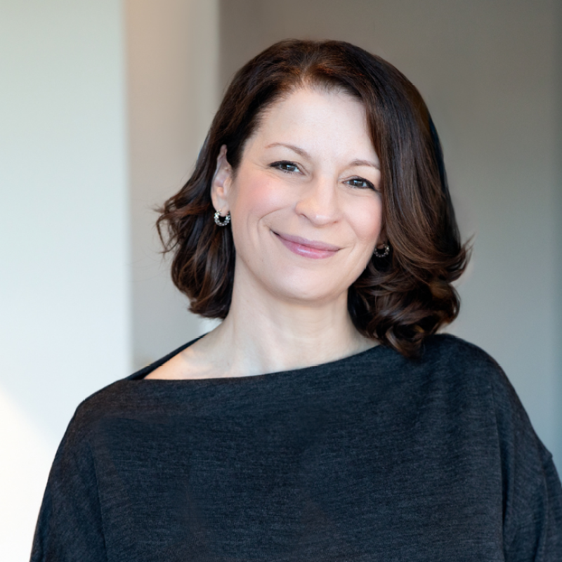 Smiling woman in a dark gray top, standing against a light background.