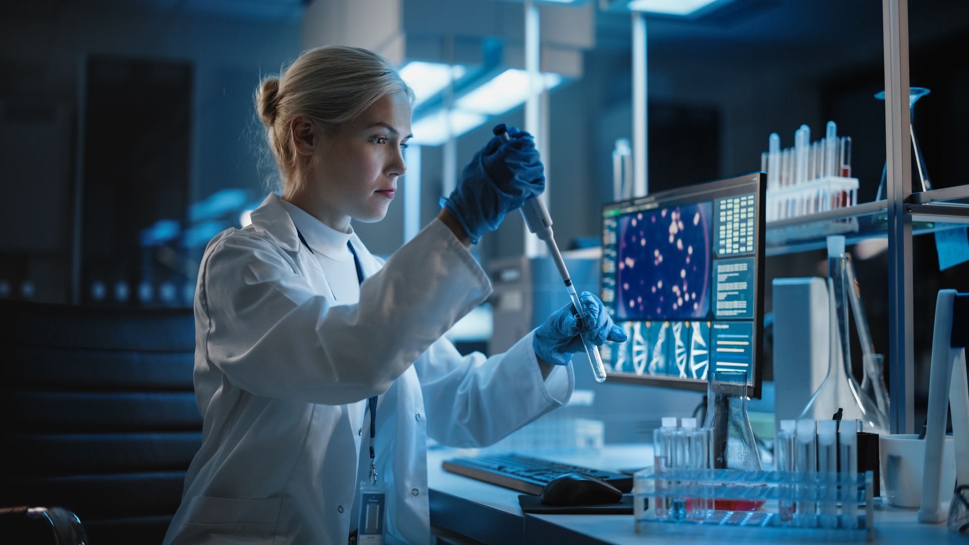 Scientist in a lab examining a digital data display beside test tubes and lab equipment