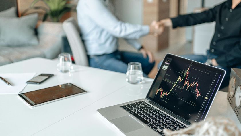 Laptop with stock chart on a white office table, with people shaking hands in the blurred background