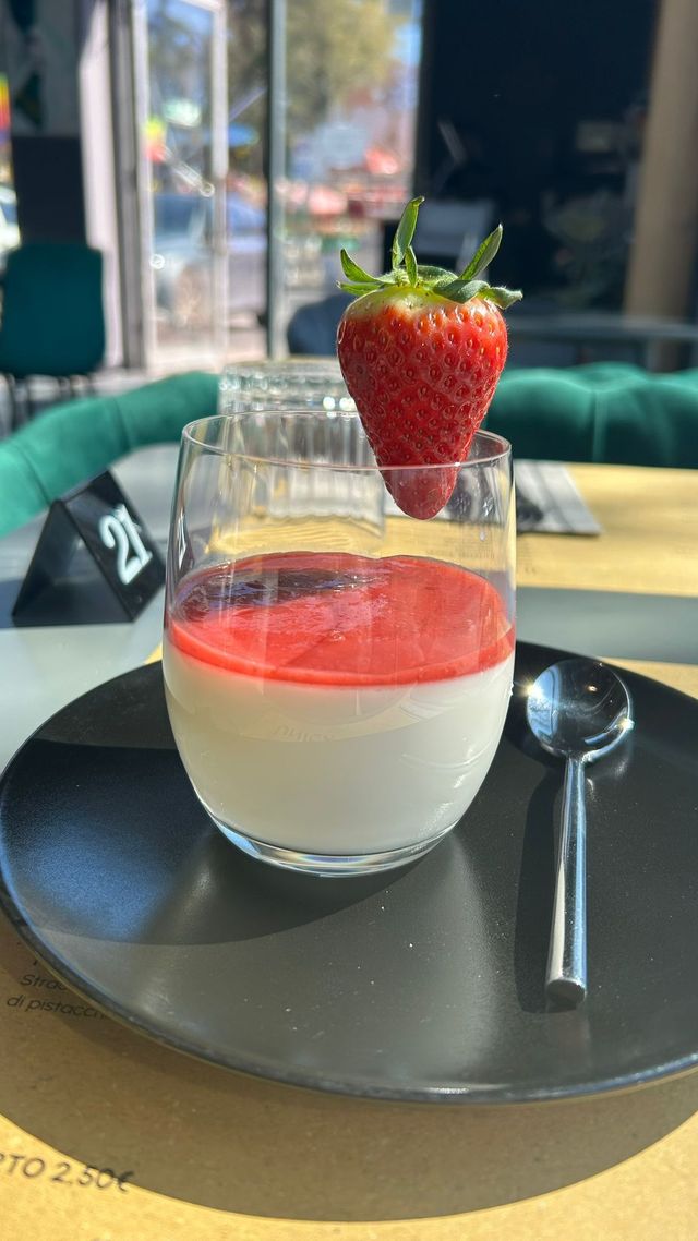 Dessert con fragole in un bicchiere su un piatto nero, con un cucchiaio sul tavolino di un caffè.