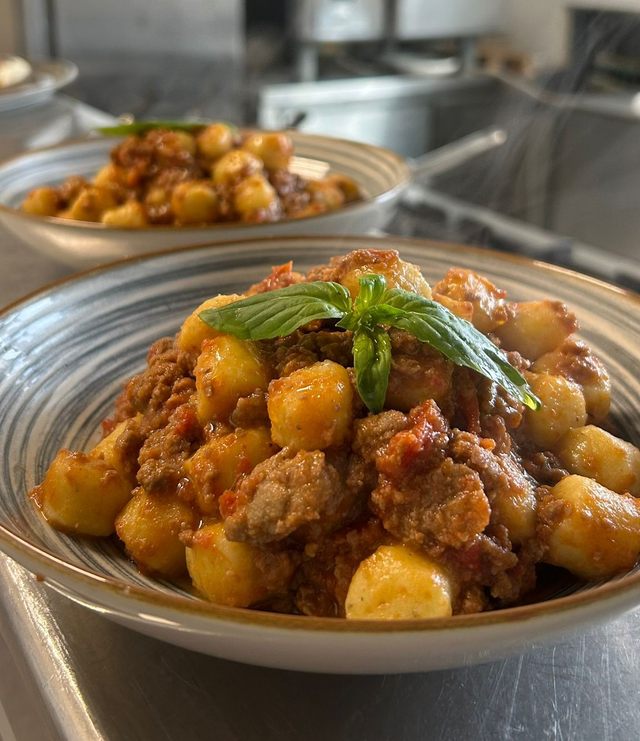 Due piatti di gnocchi al sugo con carne e basilico su un tavolo