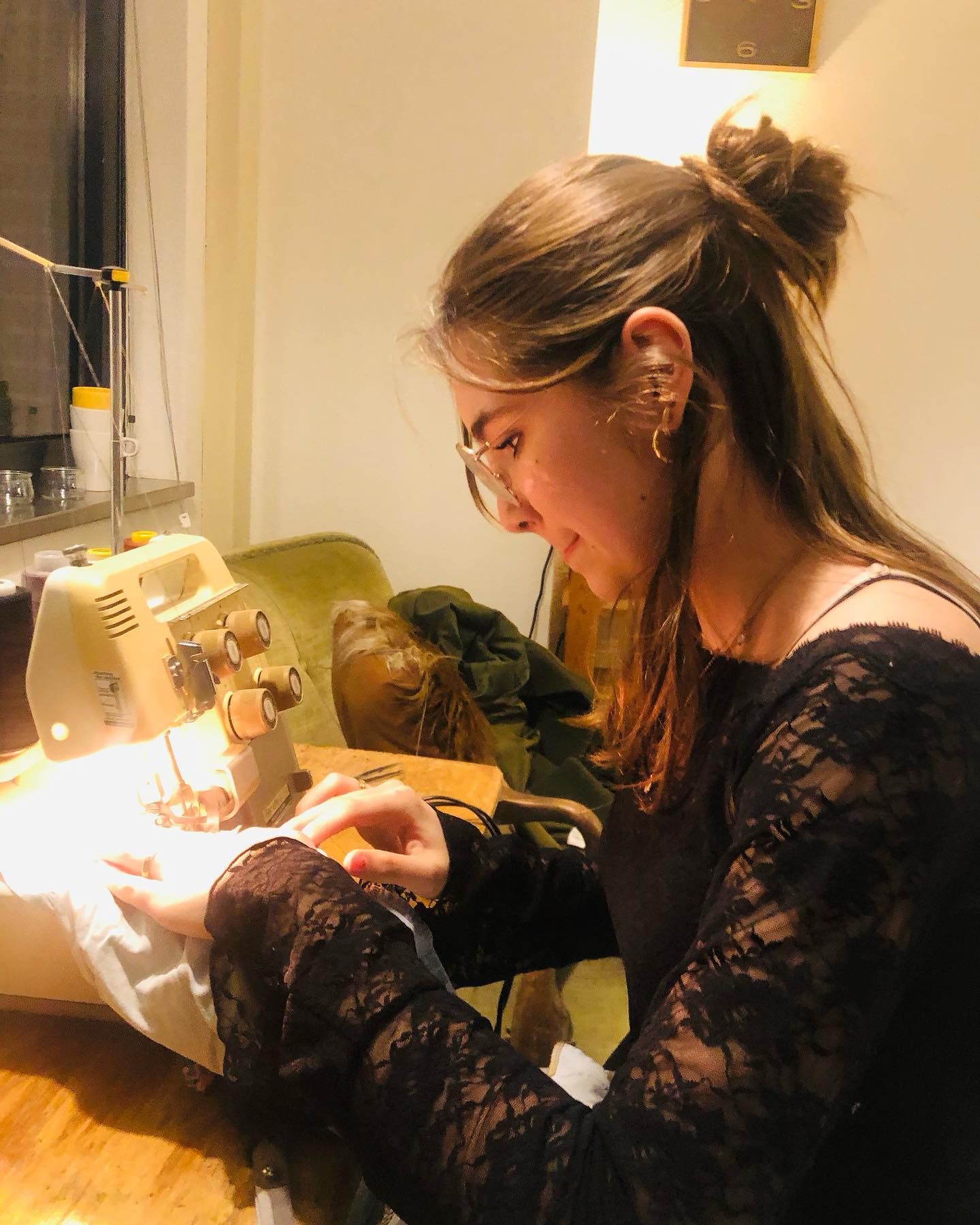 Vrouw met bril naait stof op een naaimachine, binnenshuis.