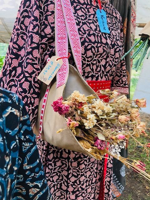 Een beige tas gevuld met gedroogde bloemen hangt aan een paspop die een jurk met bloemenprint draagt.