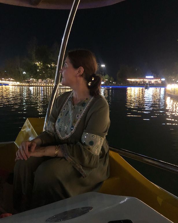 Vrouw in een boot op het water 's nachts, kijkend naar lichtjes. Ze draagt ​​een groene jurk met zilveren details.
