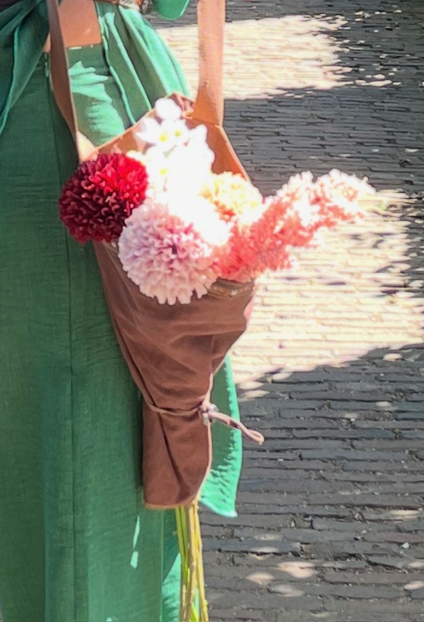 Een persoon in een groene jurk draagt ​​een bruine leren bloementas gevuld met kleurrijke bloemen.