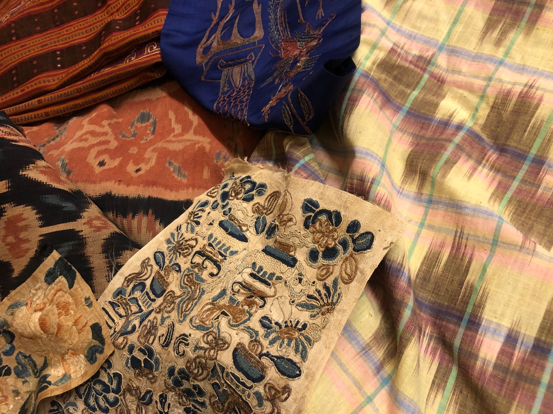 Een stapel kleurrijke textielstoffen: bruin, blauw, oranje en geruite patronen.