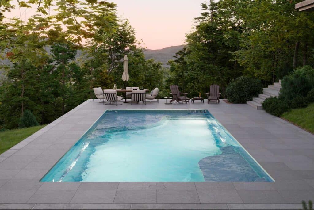 Backyard pool at dusk with lounge chairs and trees around a lit blue water feature