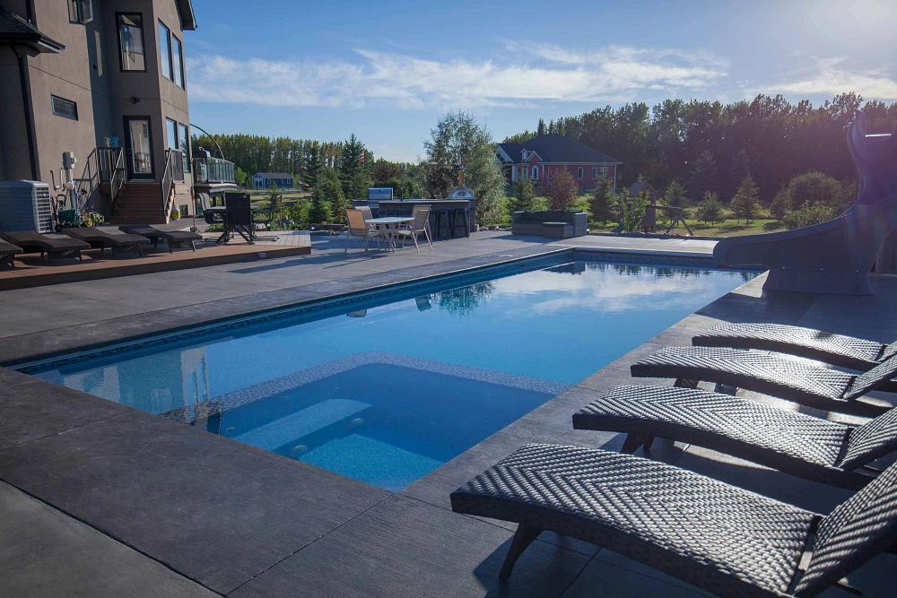 Outdoor swimming pool with blue water, black lounge chairs, and apartment buildings in the background
