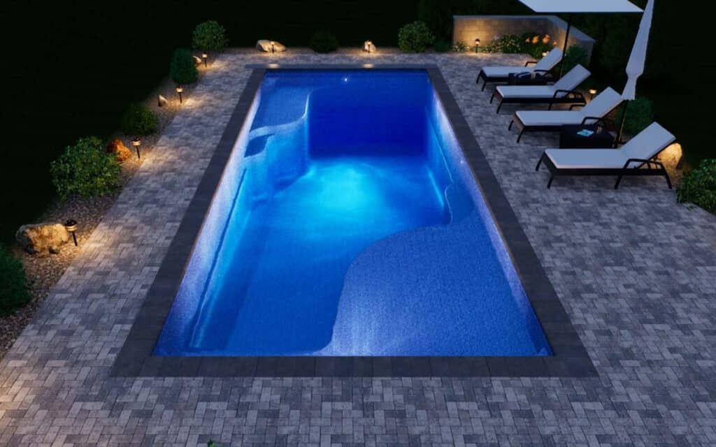 Illuminated backyard pool at night with lounge chairs and landscaping