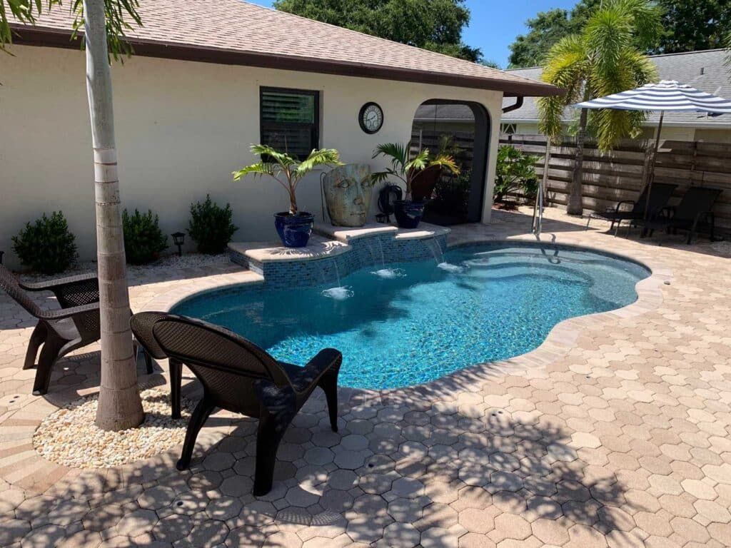Backyard pool beside a white house with lounge chairs and a shaded patio