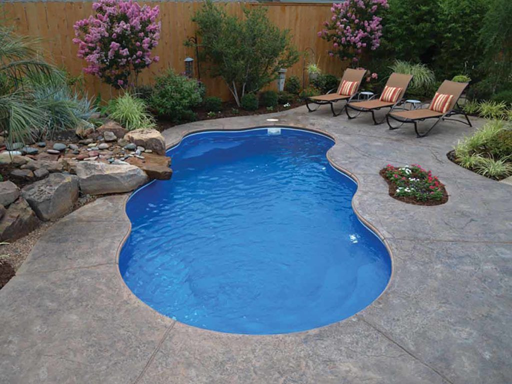 Small backyard swimming pool with blue water, stone patio, lounge chairs, and landscaped garden around it