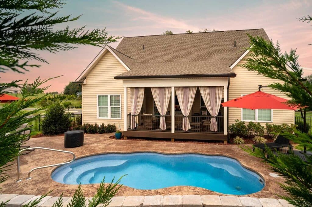 Backyard patio with a house, blue pool, and red umbrellas at sunset