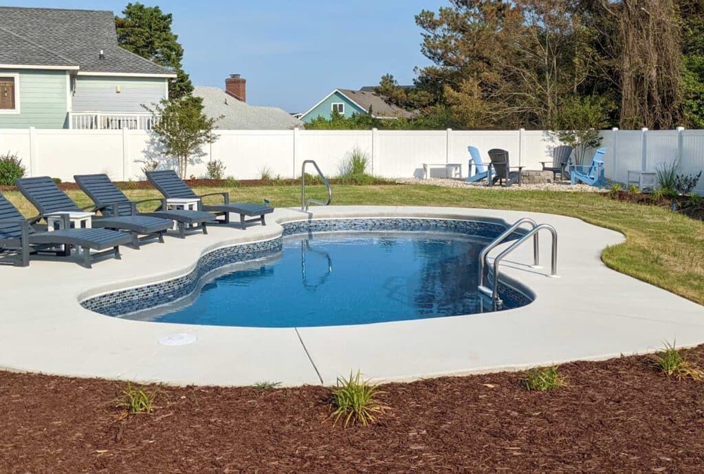 Backyard pool with blue water, lounge chairs, white fence, and patio seating on a sunny day