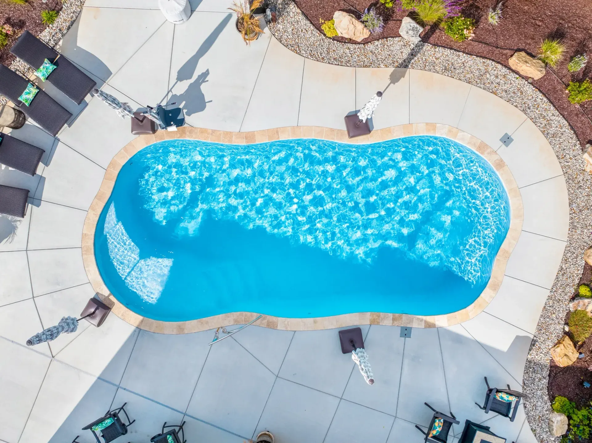 Aerial view of a blue swimming pool surrounded by tan patio tiles and lounge chairs.