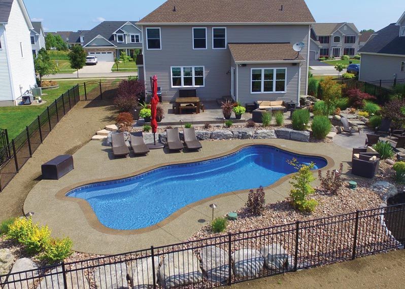 Backyard with freeform blue swimming pool, lounge chairs, patio, and a two-story house behind it