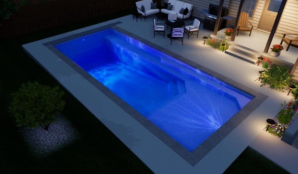 Lit backyard swimming pool with bright blue water beside a patio and outdoor seating at night