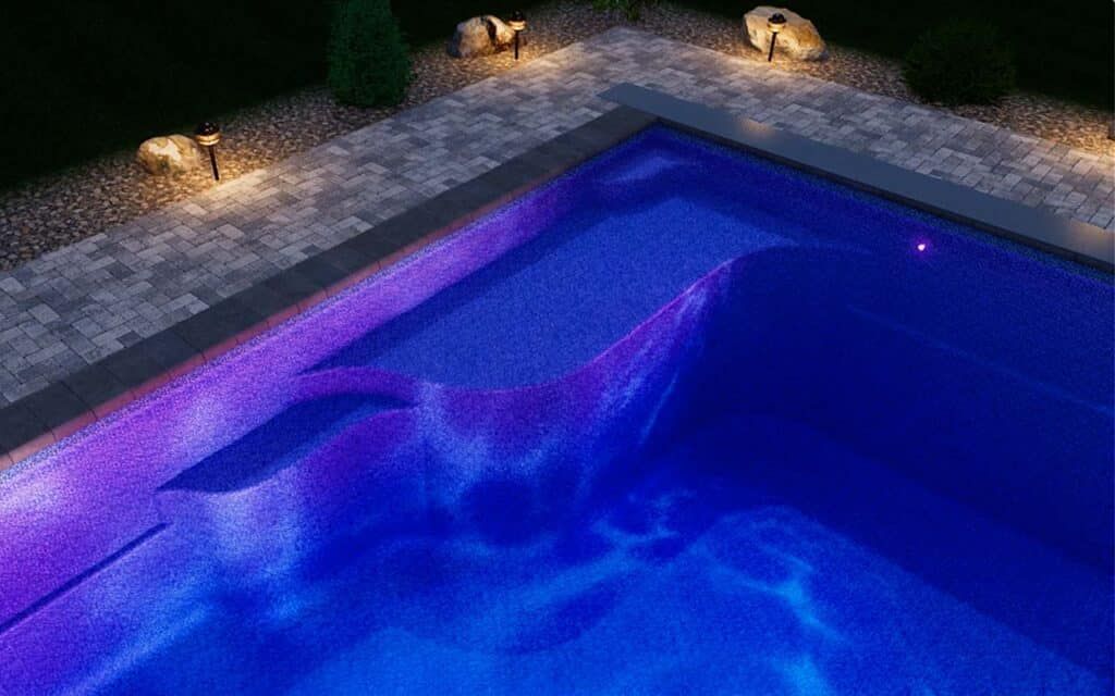 Lit backyard swimming pool at night with blue water, purple underwater lighting, and stone deck lamps