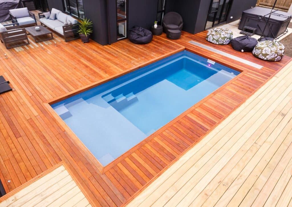 Rectangular backyard pool with blue water, surrounded by a wooden deck and outdoor seating area.