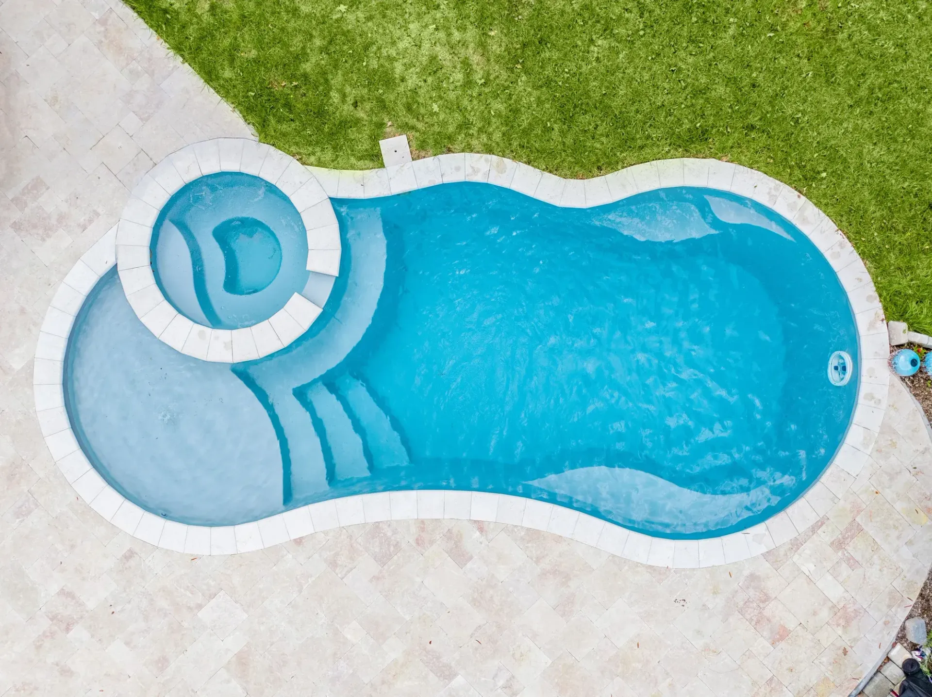 Aerial view of a blue backyard swimming pool with attached round spa on a stone patio