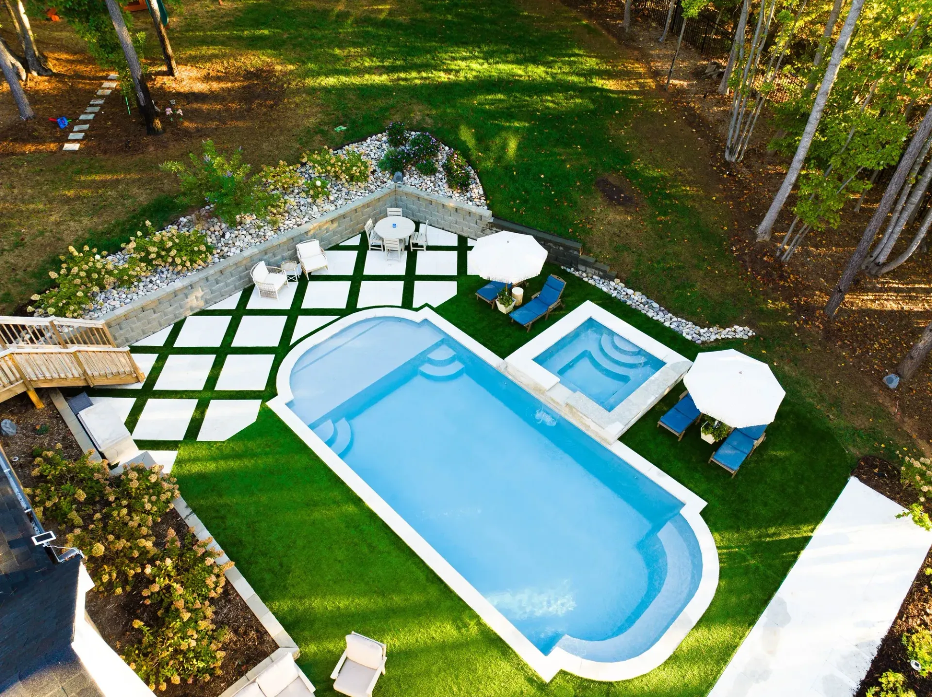Backyard with a swimming pool, hot tub, patio seating, and a checkerboard lawn design