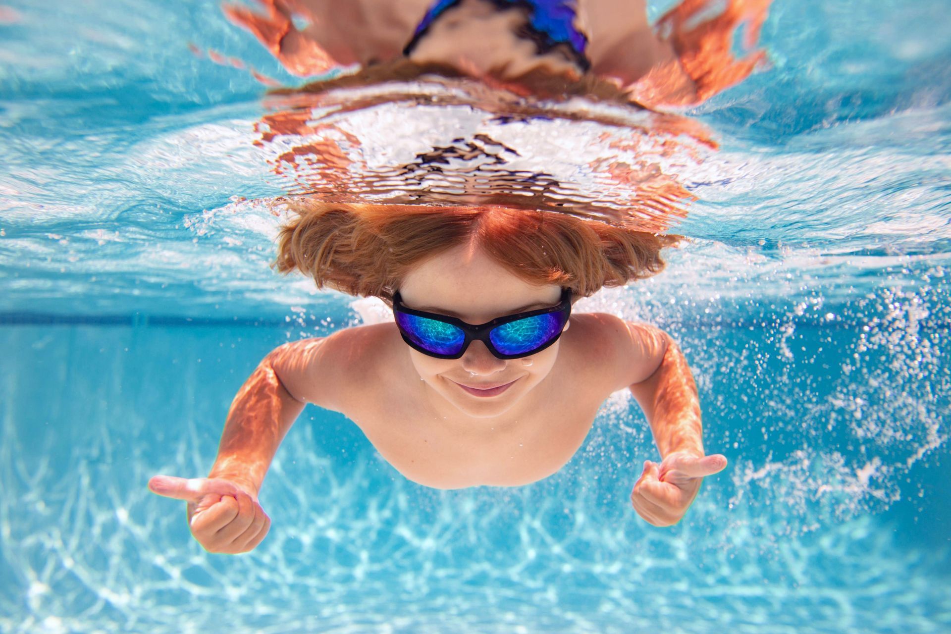Child swimming underwater with blue goggles in a bright pool