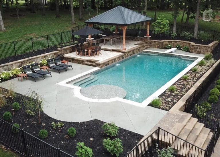 Backyard swimming pool with lounge chairs, patio seating, and a shaded gazebo on a stone deck