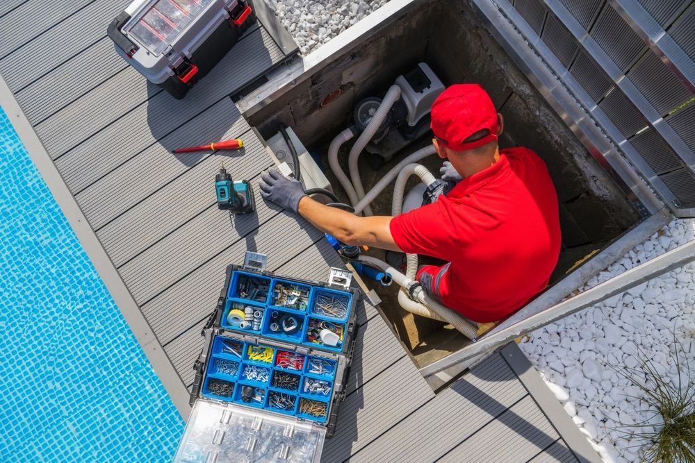 Worker in red uniform using a hose while standing on a rooftop near an open hatch and tool crate