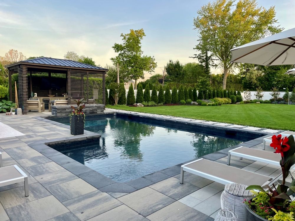 Modern backyard pool with lounge chairs, patio, and landscaped garden beside a small pavilion.