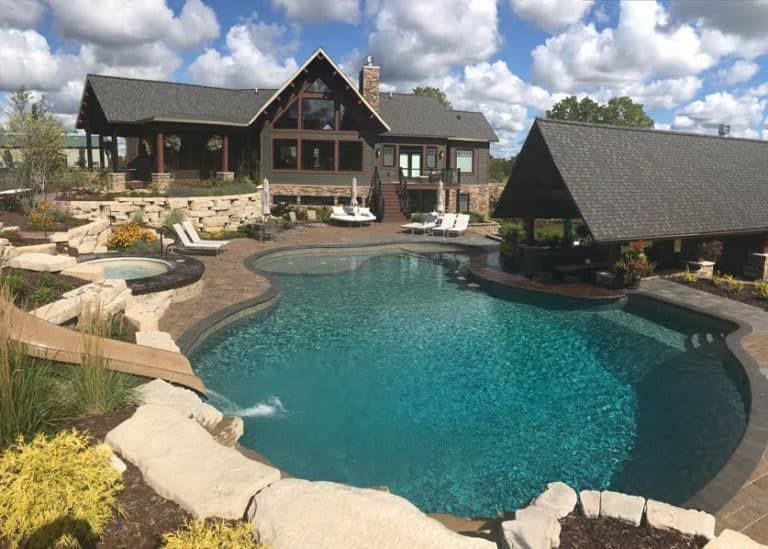 Luxury backyard with a freeform turquoise pool, stone patio, and large cabin-style house