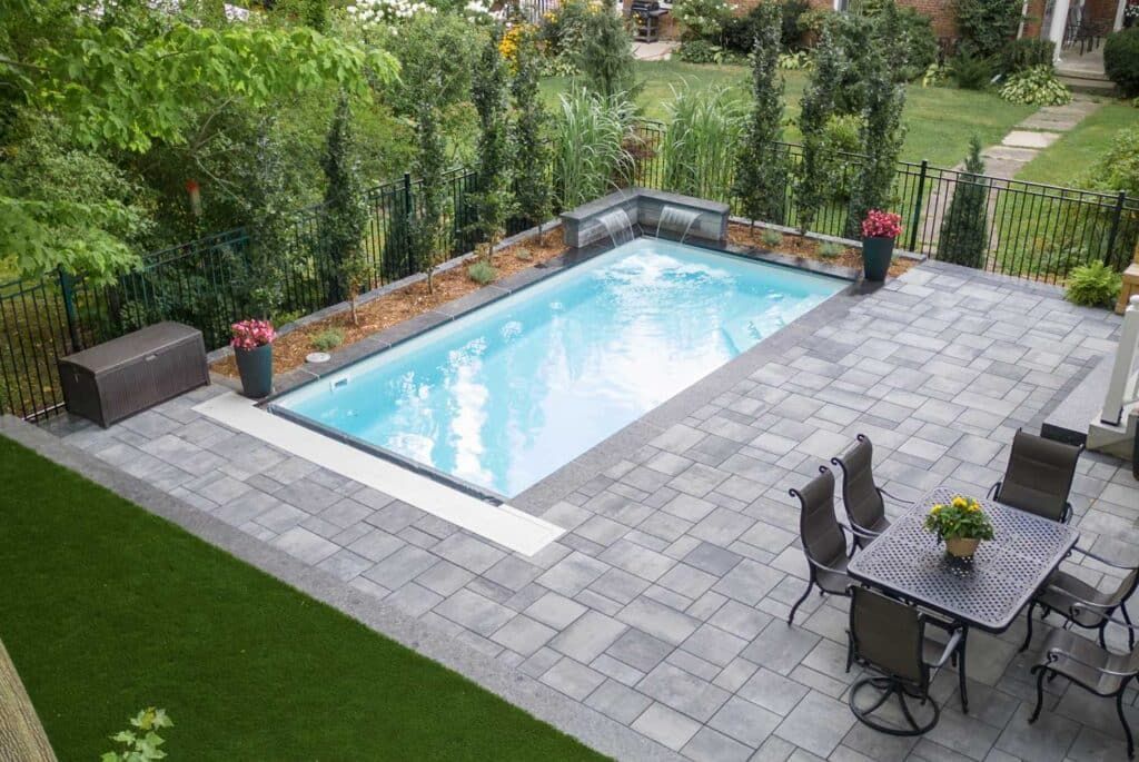 Backyard with rectangular swimming pool, stone patio, outdoor dining table, and surrounding greenery