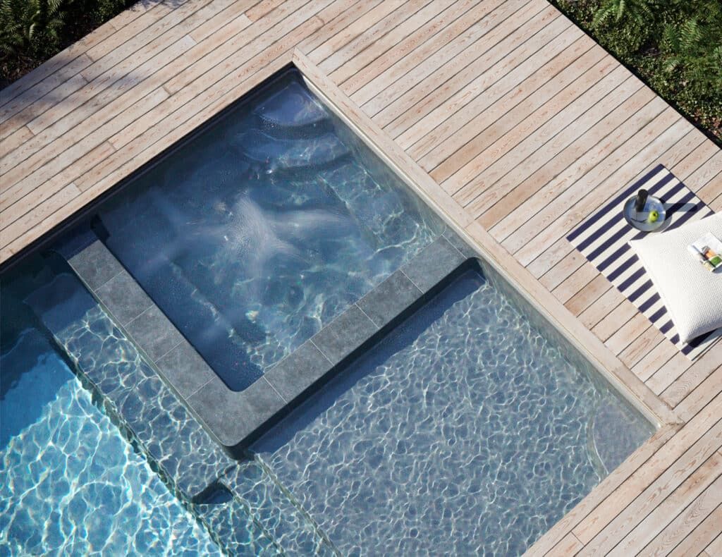 Modern pool with square hot tub, blue water, and light wood deck with lounge chair