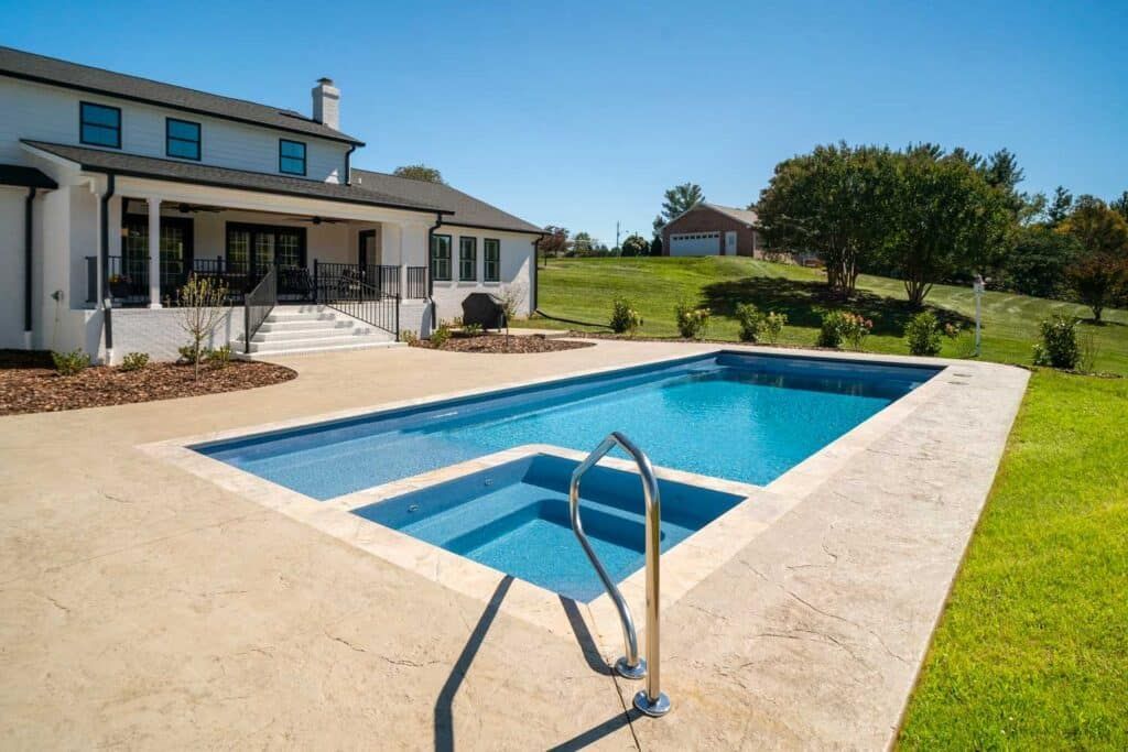 Backyard swimming pool beside a white house on a sunny day